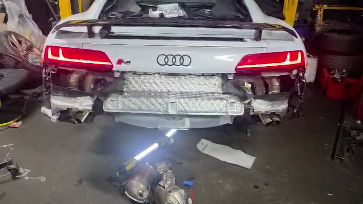 Audi R8 V10 with the rear bumper removed in a workshop, showing the four exhaust outlets and the R8 badge