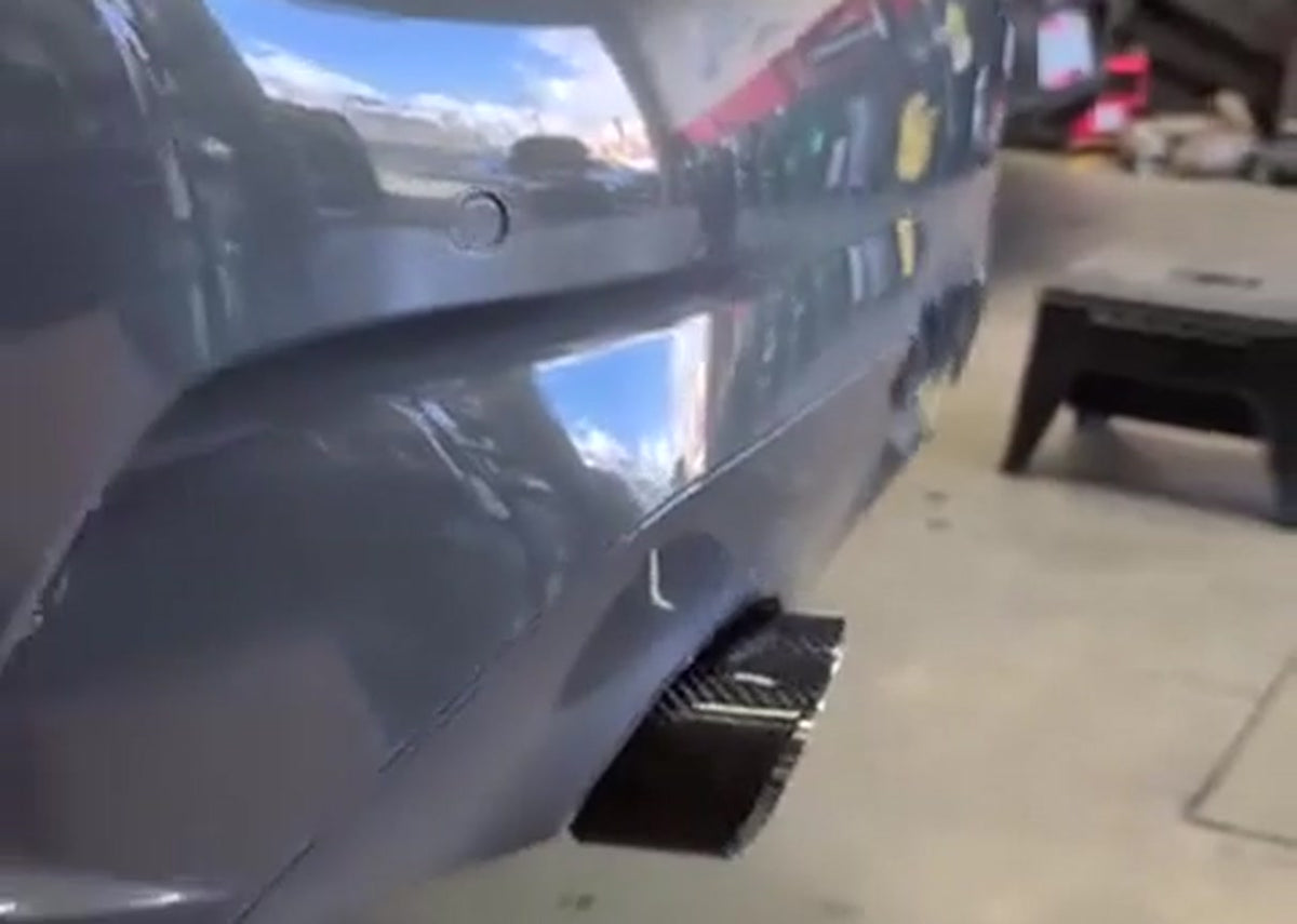 Graphite grey BMW G20 330i rear in a workshop, boot open with a carbon fibre rear diffuser and dark-finished exhaust tips