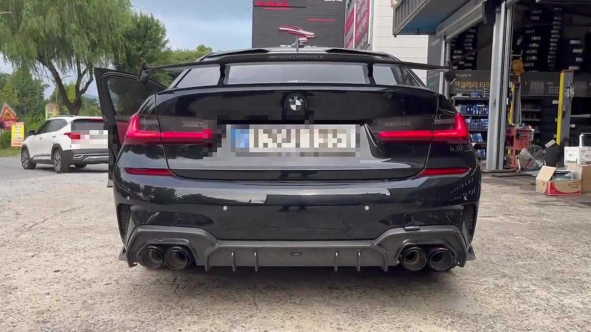 Black BMW M340i G20 rear view in a Korean workshop, M Performance-style wing, carbon diffuser with four black exhaust tips, number plate pixelated for privacy