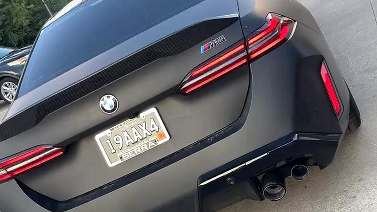 BMW M5 G90 (G90/G99) rear three-quarter on the road, titanium valved catback fitted, no number plate visible in frame