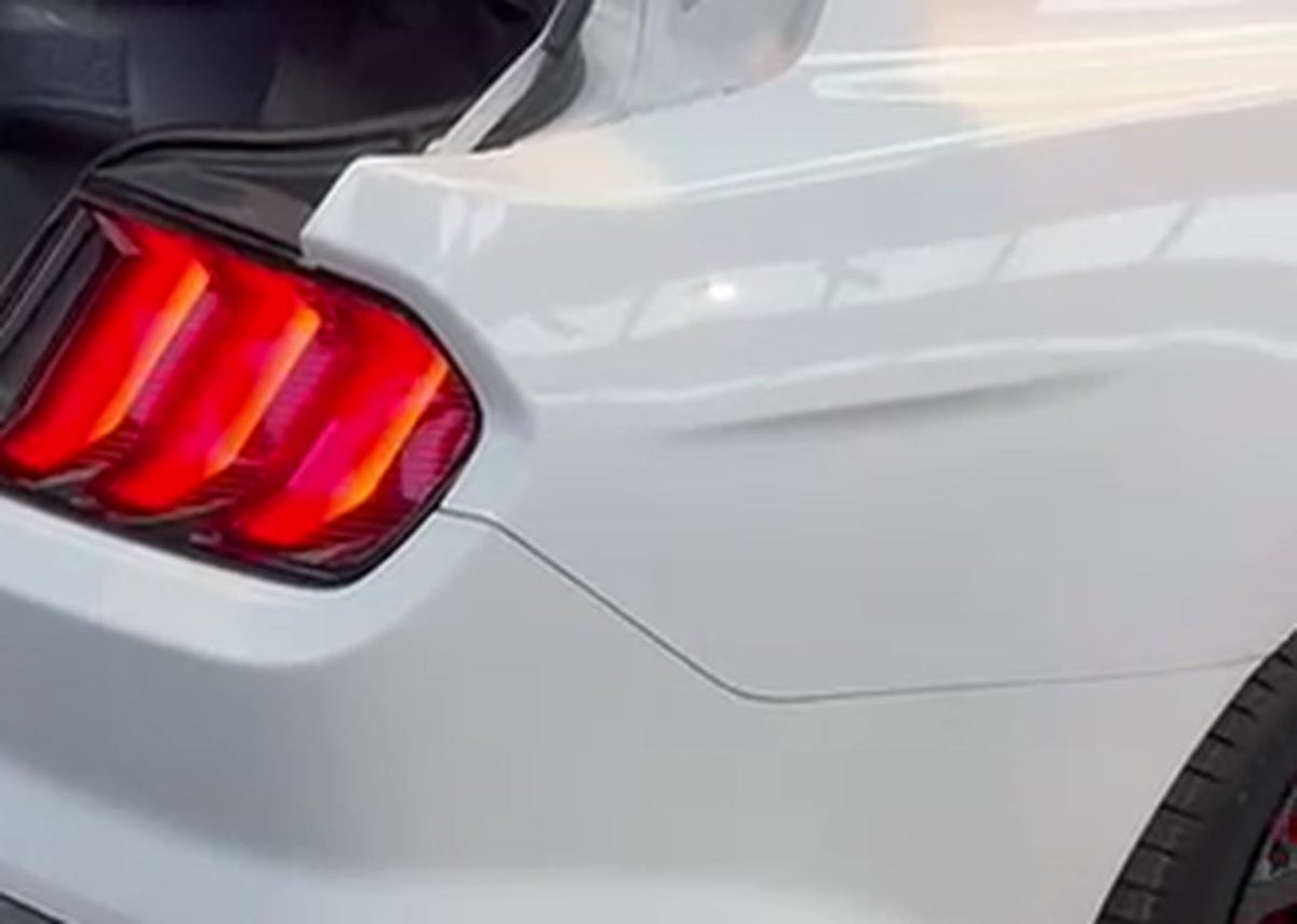 White Ford Mustang GT S550 rear quarter in a workshop, signature triple-bar tail light lit, boot open during the exhaust installation
