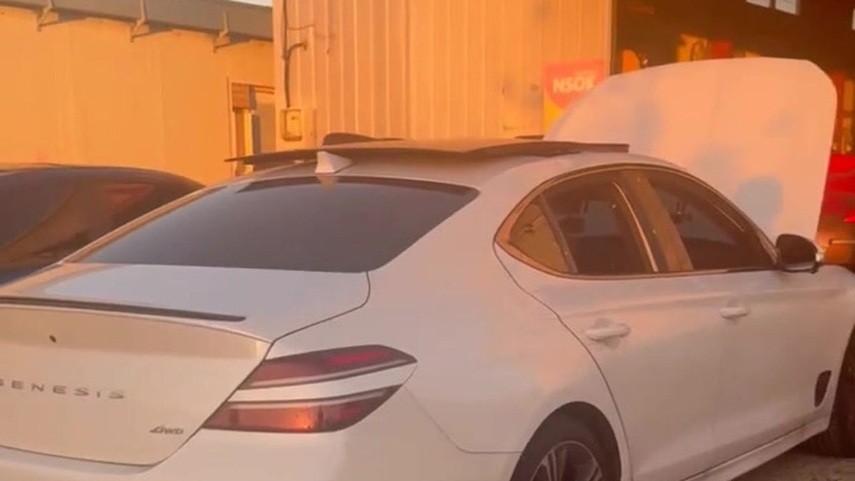 White 2025 Genesis G70 3.3T seen from the rear three-quarter outside a workshop at golden hour, tail lights lit, showing the GENESIS and 4WD rear badges