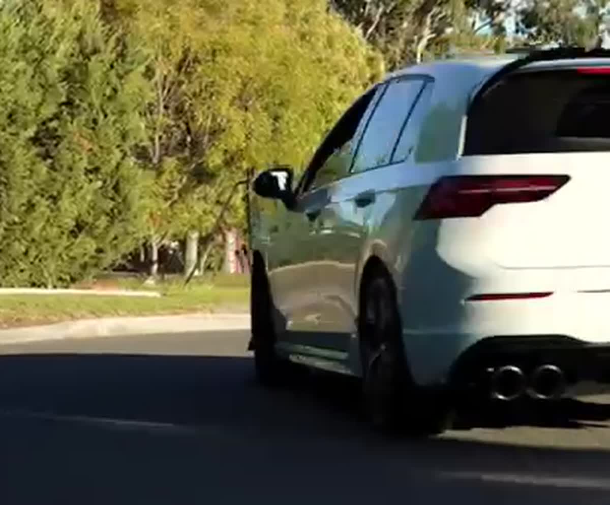 White Volkswagen Golf R Mk8 on a suburban street, rear three-quarter view showing the quad exhaust tips and the black rear diffuser